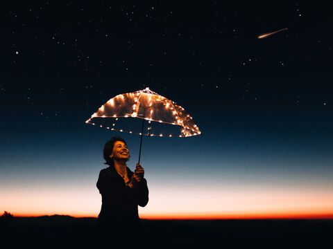 Frau mit leuchtendem Schirm, im Hintergrund Nachthimmel mit Sternschnuppe