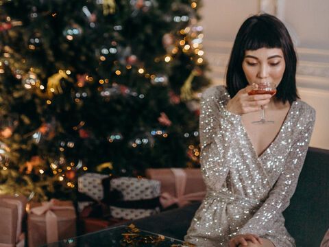 Frau sitzt in Glitzerkleid mit Getränk vor dem Weihnachtsbaum