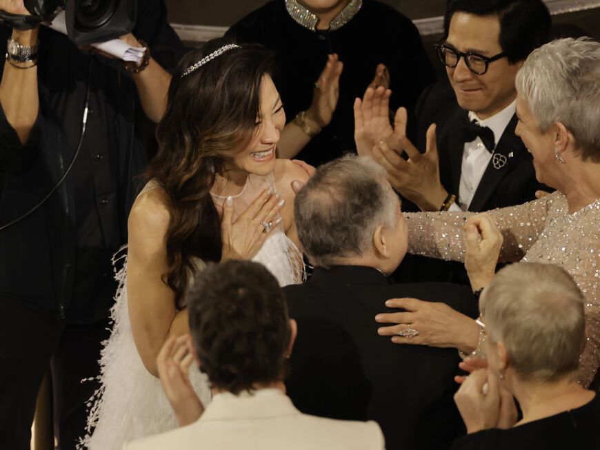 Michelle Yeoh legt die Hand auf die Brust und wird bejubelt und umarmt bei den Oscars 2023