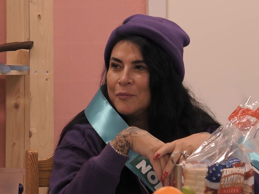 Iris Klein sitzt am Tisch bei "Promi Big Brother" und guckt ernst
