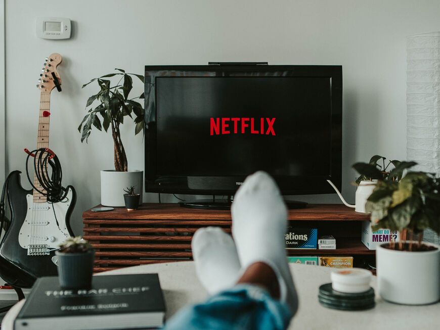 Füße liegen auf einem Couchtisch, davor steht ein Fernseher mit Netflix-Logo