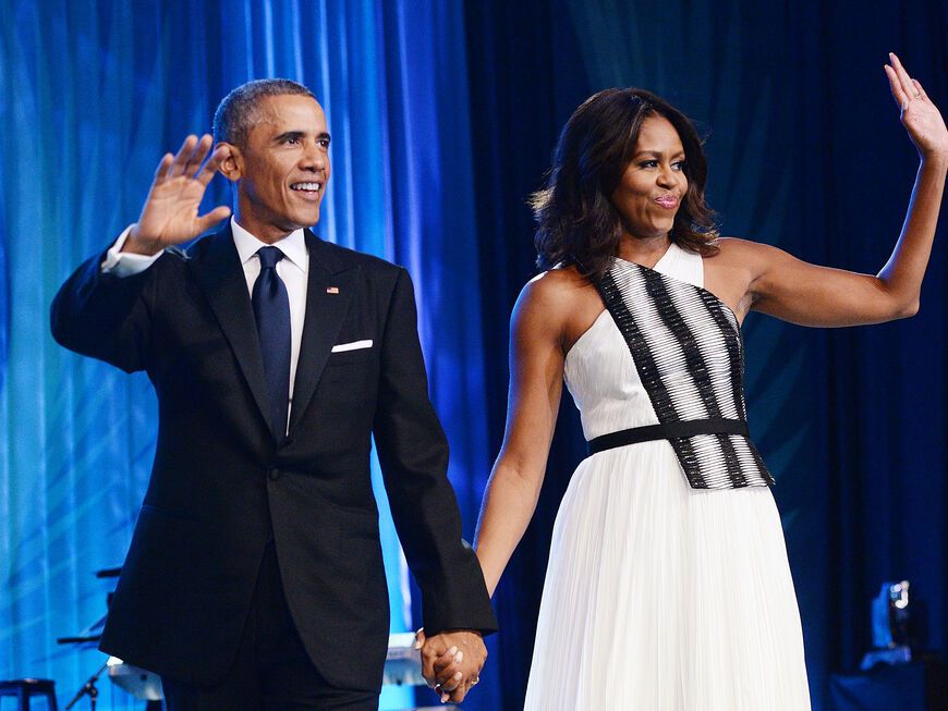 Barack und Michelle Obama winken und halten Händchen.