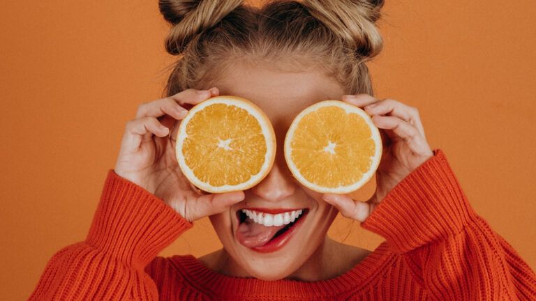Frau hält sich frische orangen vor die Augen und lacht