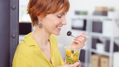 frau isst im büro einen gesunden obstsalat