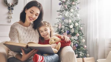 Mutter und Tochter lesen vor dem Weihnachtsbaum ein Buch zusammen