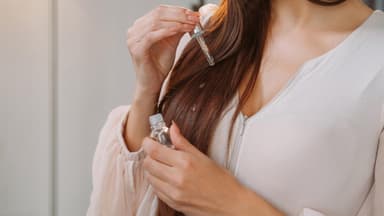 Frau trägt Haaröl auf lange braune Haare auf