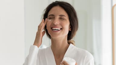Frau trägt lachend Anti-Aging-Creme auf
