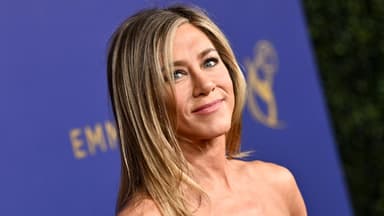 Jennifer Aniston lächelt zur Seite vor lila Wand
