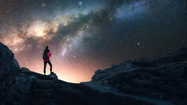 Eine Frau guckt auf einem Berg in den Sternenhimmel