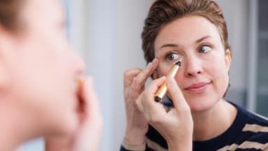 Frau trägt Concealer vor Spiegel auf