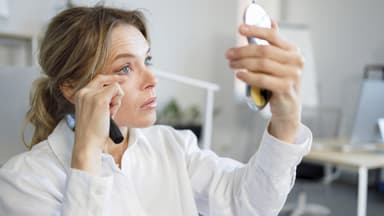 Frau mit Handspiegel schminkt wimpern