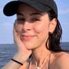 Lena Meyer-Landrut sitzt lächelnd mit Cap und Bikini am Meer