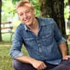 Max Müller sitzt lächelnd auf Stein im Park