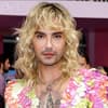 Bill Kaulitz mit blonden locken vor pinker wand