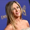 Jennifer Aniston lächelt zur Seite vor lila Wand