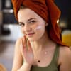Junge Frau mit Handtuch cremt sich ein