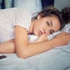 Eine junge Frau liegt traurig im Bett
