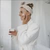 Junge Frau lächelt in Spiegel und benutzt Anti-Aging-Creme