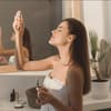 Frau sprüht Spray aufs Gesicht im Bad