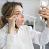 Frau mit Handspiegel schminkt wimpern