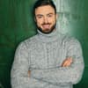 Niko Griesert steht lächelnd mit verschränkten Armen vor einer grünen Wand.