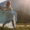 Frau tanzt in einem Kleid über eine Wiese mit Bergen im Hintergrund