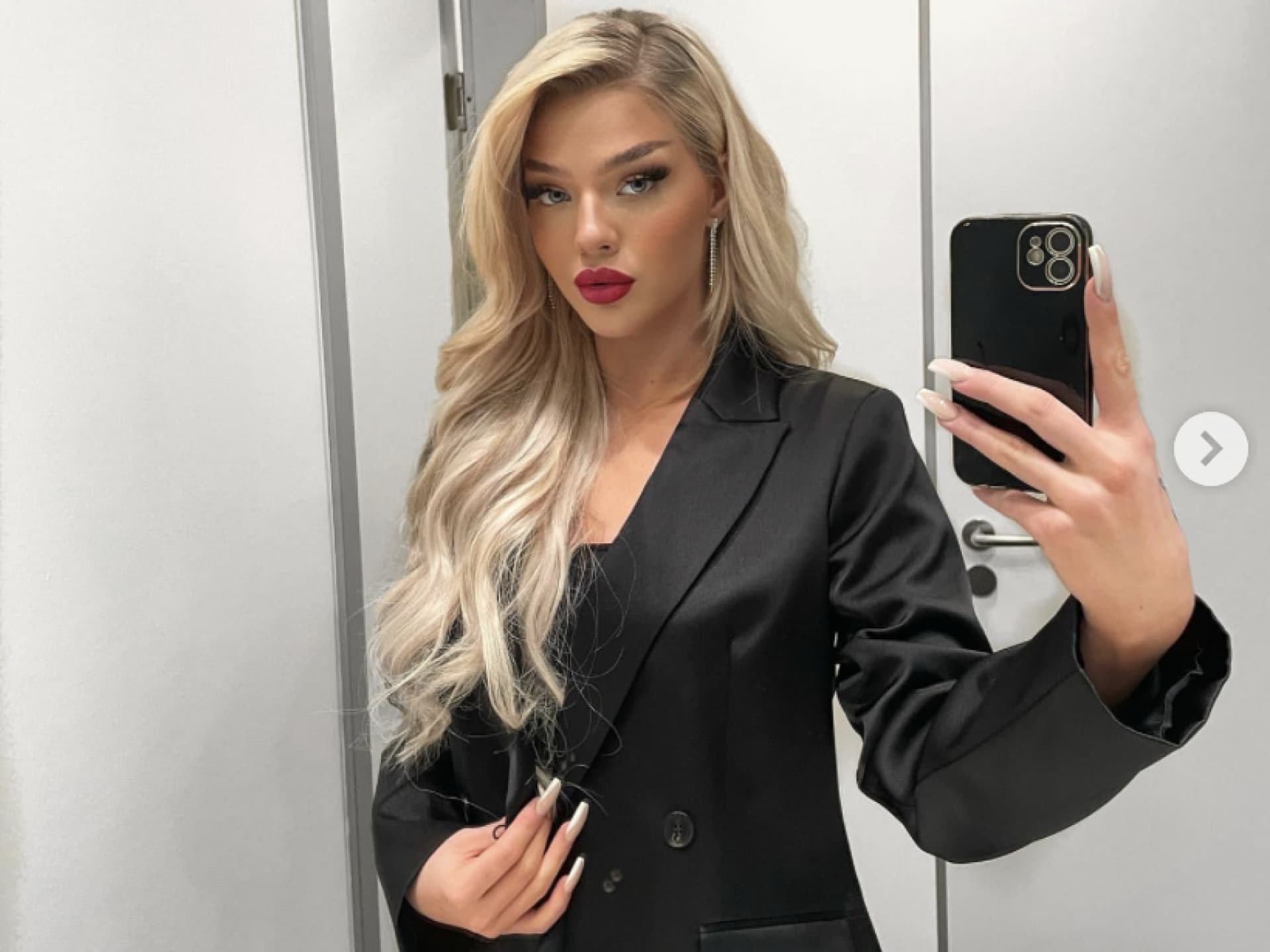 Elaine Victoria im schwarzen Blazer vorm Spiegel.