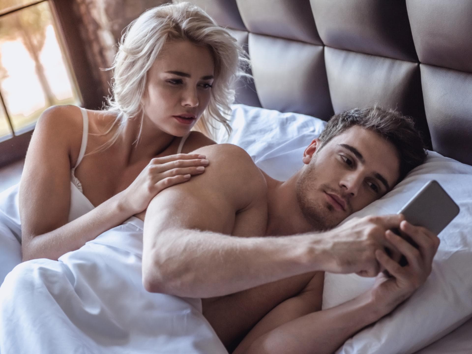 paar liegt im bett, er guckt aufs handy