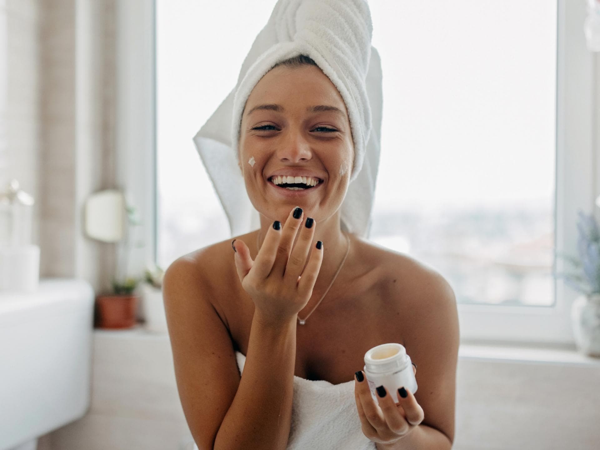 Anti-Aging-Creme für Jugend Frau cremt sich lächelnd im Handtuch ein