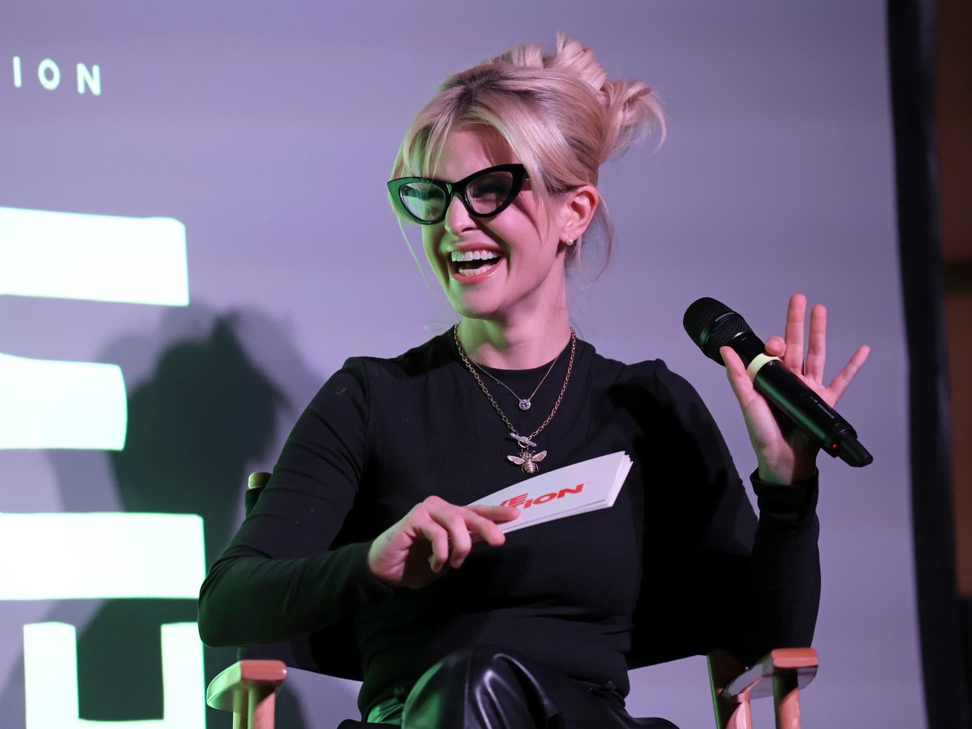 Kelly Osbourne lacht mit Brille und Mikrofon in der Hand