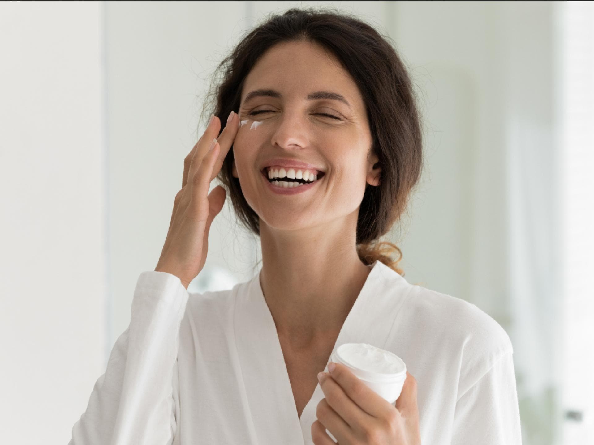 Anti-Aging-Creme Falten Frau trägt lachend Anti-Aging-Creme auf