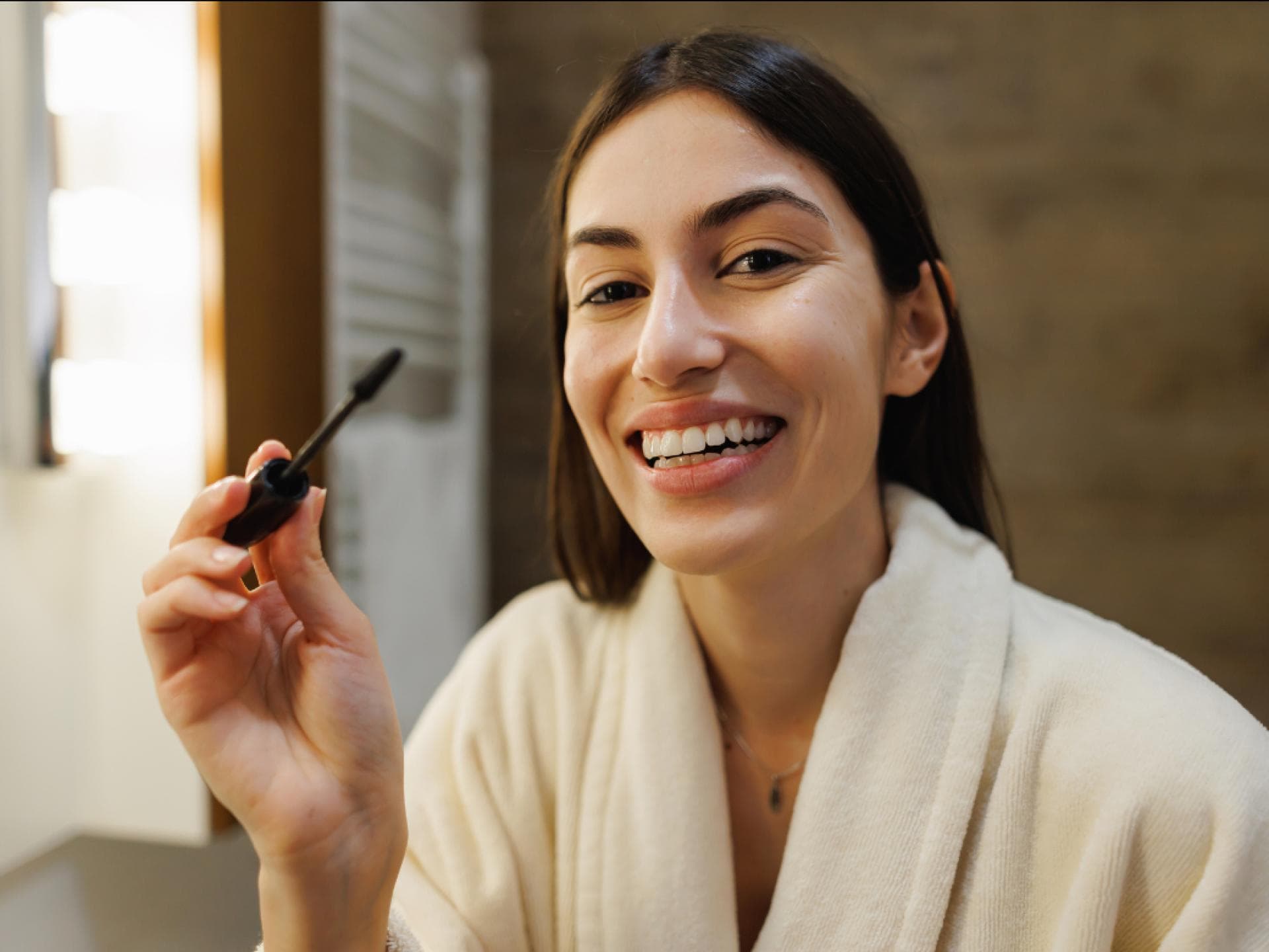 Mascara von Flaconi Frau trägt Wimperntusche im Bademantel im Bad auf