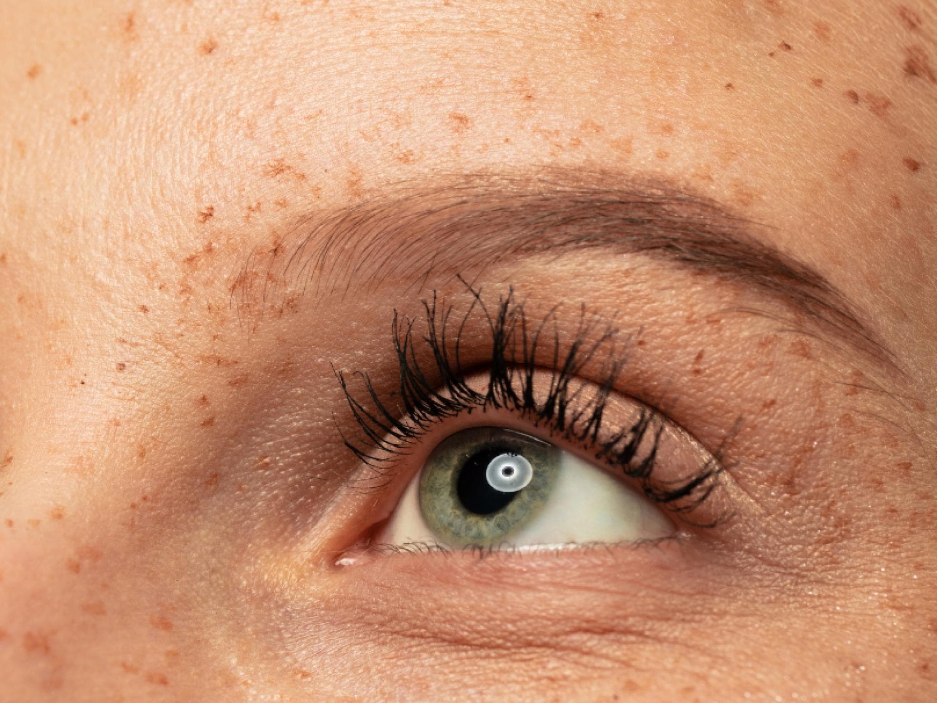 Frau mit grünen AUgen und Sommmersprossen zeigt lange Wimpern