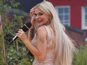 Marie Reim lacht mit Mikrofon in der Hand