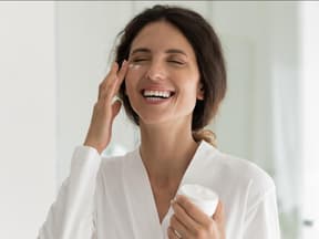 Frau trägt lachend Anti-Aging-Creme auf