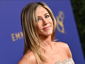 Jennifer Aniston lächelt zur Seite vor lila Wand