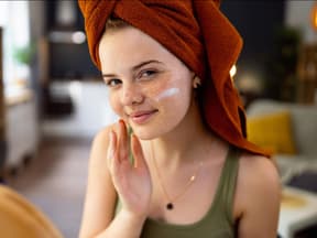 Junge Frau mit Handtuch cremt sich ein