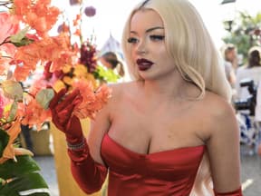 Katja Krasavice guckt ernst zur Seite, neben ihr Blumen