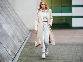 Eine Frau trägt einen grauen Jogginganzug zu einem Mantel in Beige