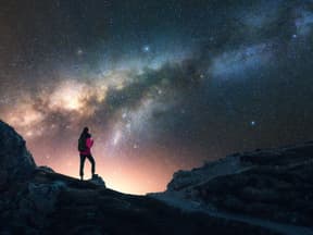 Eine Frau guckt auf einem Berg in den Sternenhimmel