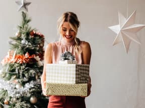 Frau mit Weihnachtsgeschenken vor Tannenbaum