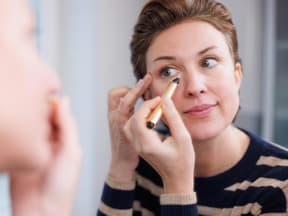 Frau trägt Concealer vor Spiegel auf