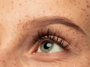 Frau mit grünen AUgen und Sommmersprossen zeigt lange Wimpern