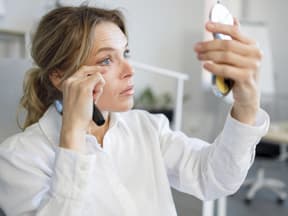 Frau mit Handspiegel schminkt wimpern
