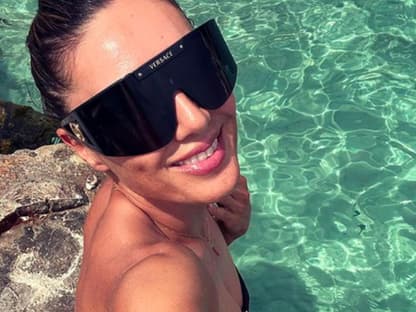 Nazan Eckes sitzt am Meer und lacht mit Sonnenbrille
