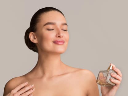 frau sprüht sich mit parfum ein und genießt den Duft