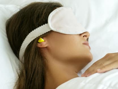 Besten Ohrstöpsel von Stiftung Warentest Frau mit Ohrstöpsel und Schlafmaske im Bett