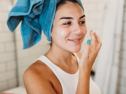 Anti-Aging mit Retinol-Alternative Frau mit Handtuch-Turban cremt Gesicht ein