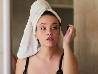 Pflegende Mascara Frau vor Spiegel tuscht Wimpern