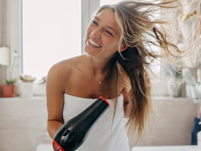 Föhnspray für mehr Volumen Frau föhnt Haare